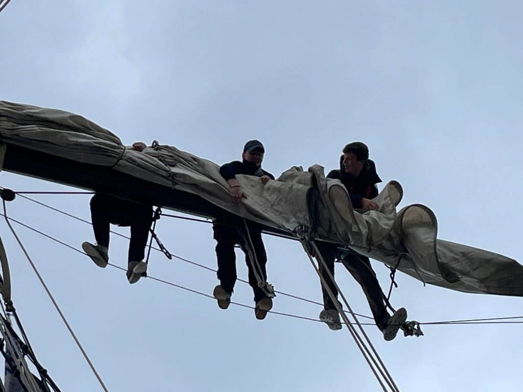Schüler*innen falten das Segel auf dem Mast.