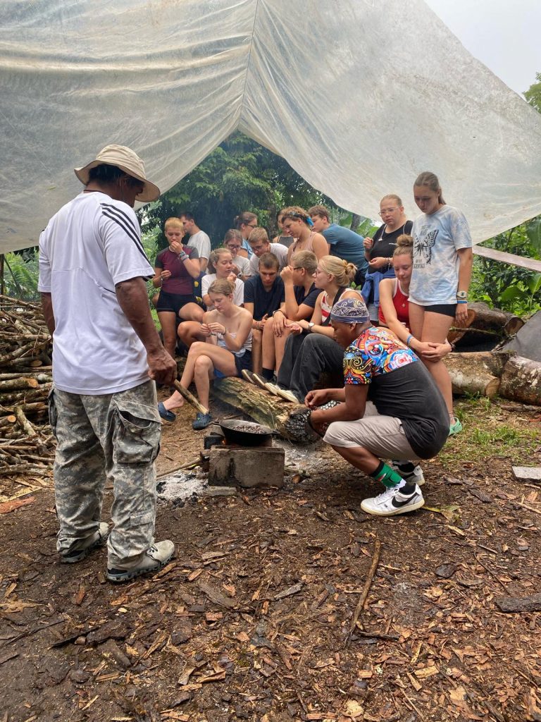 Schüler sitzen versammelt um Kakaobohnen, die erhitzt werden.