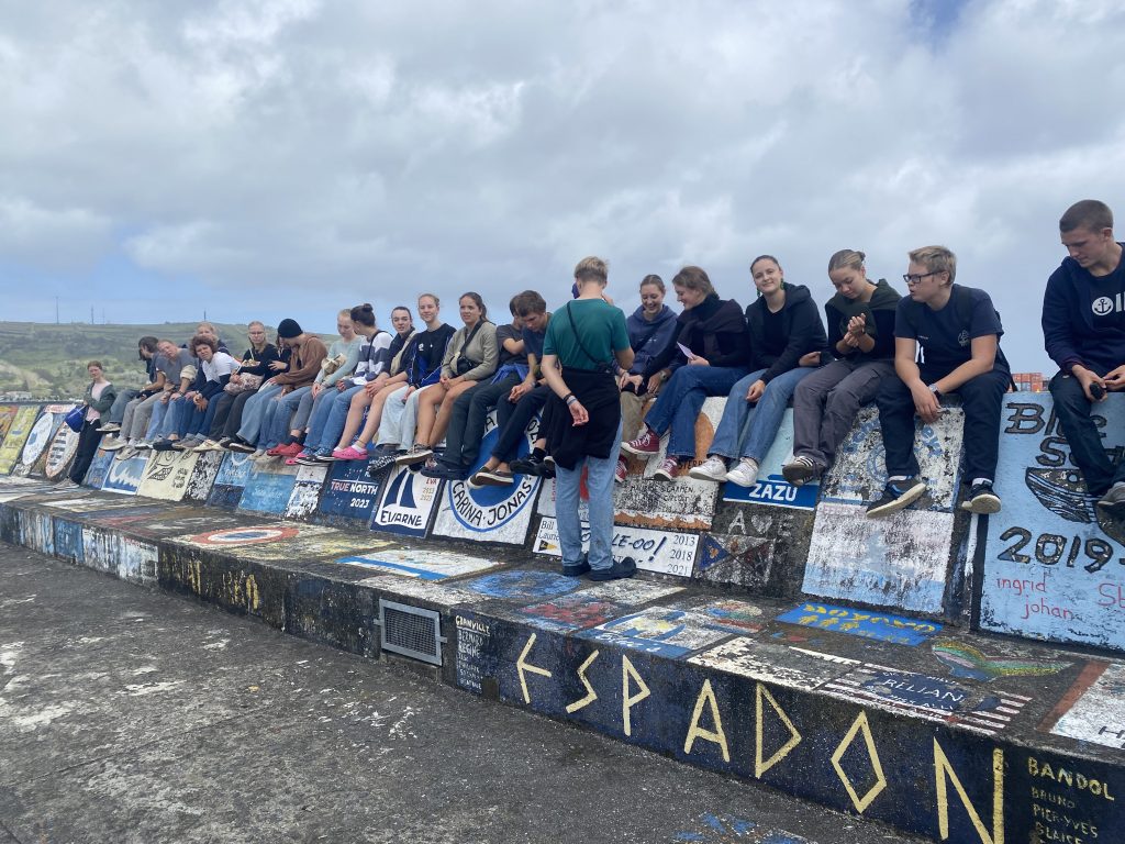 Schüler*innen sitzen auf der Hafenmauer der Azoren.